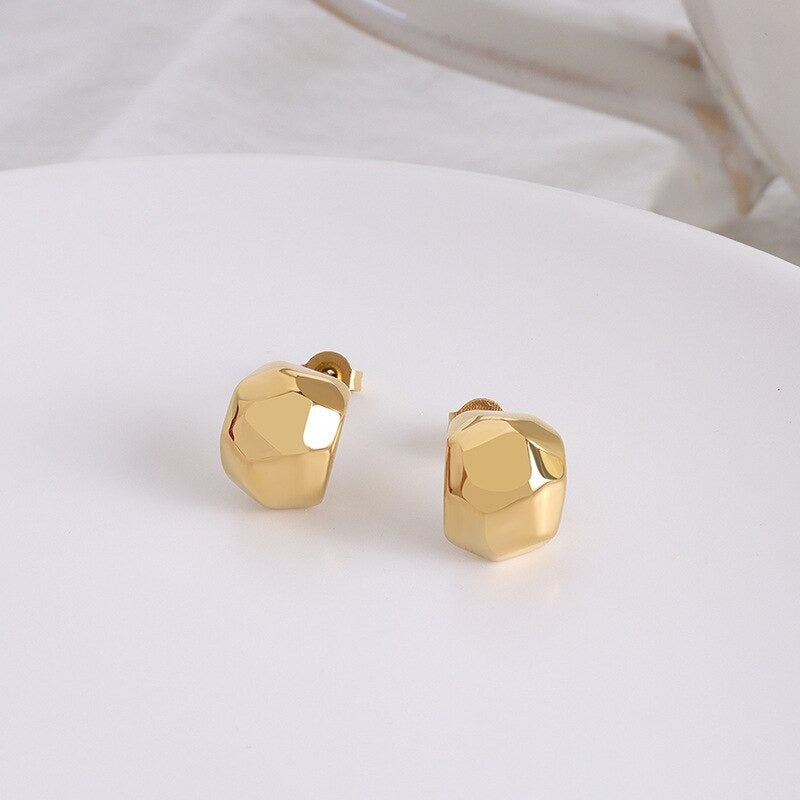 Gold Zani Faceted Earrings laying on a smooth white surface.