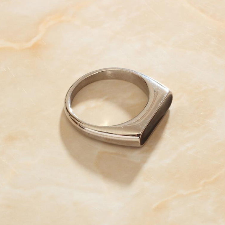 Silver Long Black Set Signet Ring on a smooth marble surface.