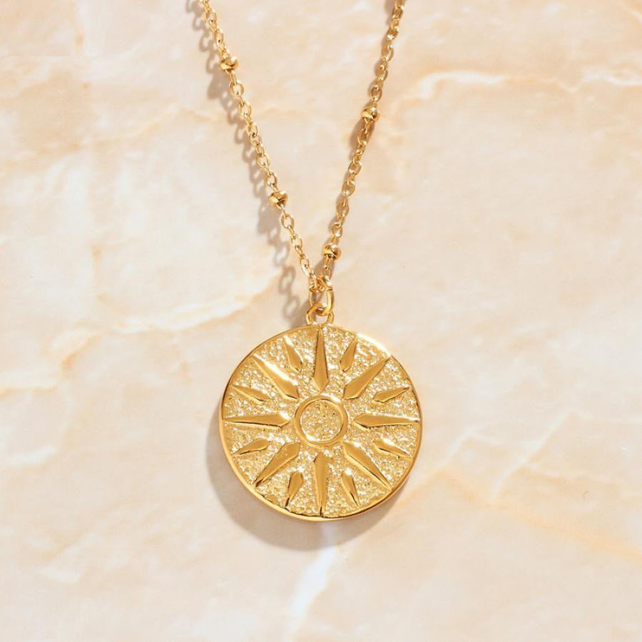 Gold Sun Ra Three Chain Pendant Necklace laying on a light coloured marble background.
