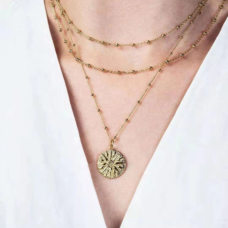 A gold three chain Sun Ra necklace hanging on a woman's neck with a white blouse.